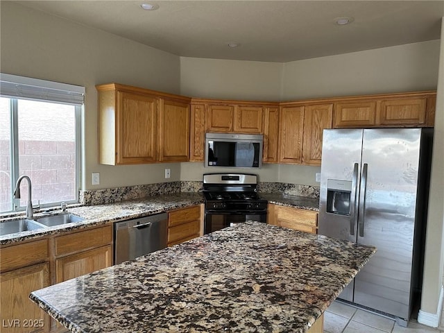 kitchen with light tile patterned flooring, a kitchen island, a sink, appliances with stainless steel finishes, and dark stone counters