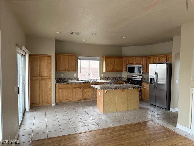 kitchen with a center island, light tile patterned floors, visible vents, appliances with stainless steel finishes, and dark stone countertops