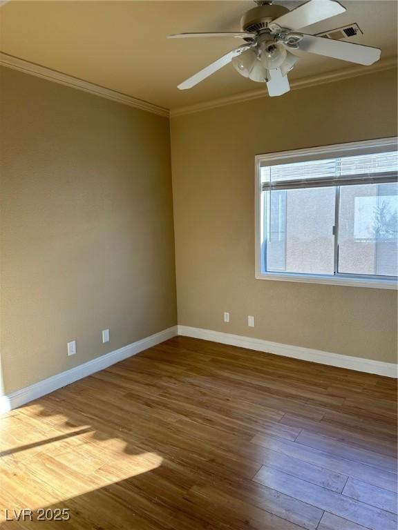 spare room featuring wood finished floors, a ceiling fan, visible vents, baseboards, and ornamental molding