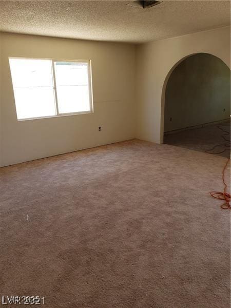 unfurnished room with carpet, arched walkways, and a textured ceiling