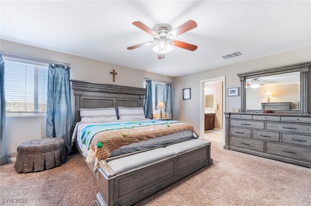 bedroom featuring a ceiling fan, light colored carpet, visible vents, and ensuite bath