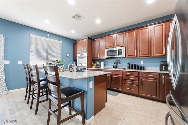 kitchen featuring light tile patterned floors, a center island with sink, visible vents, a breakfast bar area, and stainless steel appliances