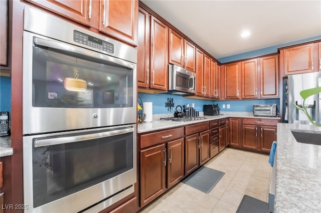 kitchen with stainless steel appliances, light stone countertops, a toaster, and light tile patterned floors