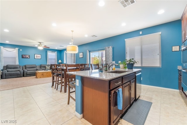 kitchen with light tile patterned floors, a sink, visible vents, light stone countertops, and dishwasher