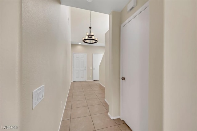 hallway featuring light tile patterned flooring, baseboards, and an inviting chandelier