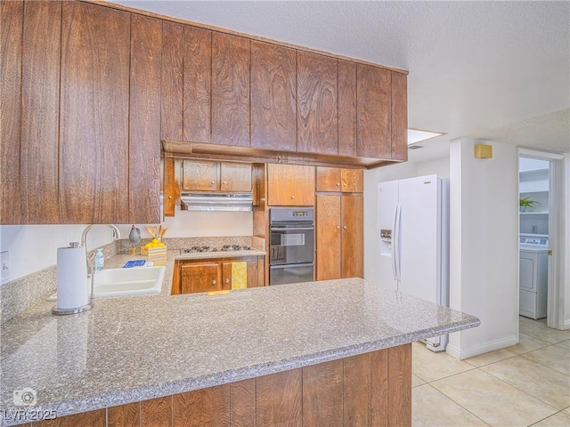 kitchen with oven, under cabinet range hood, a peninsula, white fridge with ice dispenser, and washer / dryer