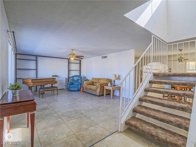 living room with a textured ceiling, light tile patterned flooring, visible vents, a ceiling fan, and stairway