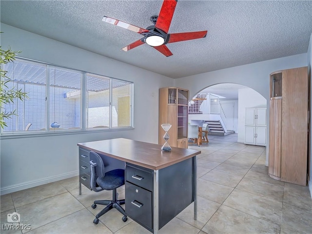 home office with arched walkways, ceiling fan, a textured ceiling, and light tile patterned flooring