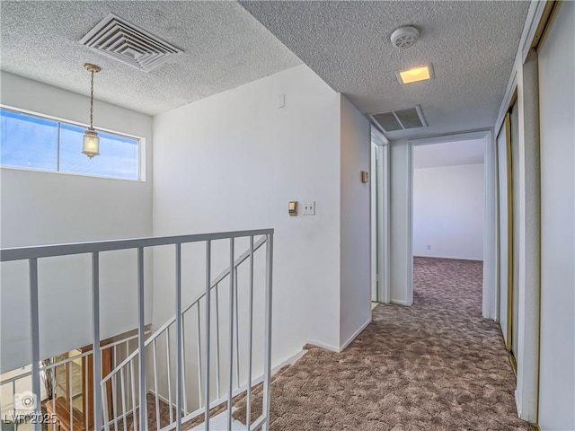 hall with carpet, visible vents, a textured ceiling, and an upstairs landing