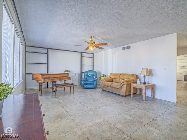 living room featuring a ceiling fan, light tile patterned floors, visible vents, and a textured ceiling