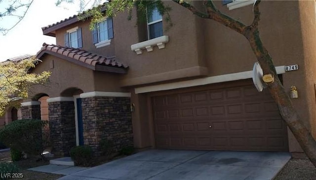 mediterranean / spanish-style house featuring a garage, a tile roof, concrete driveway, stone siding, and stucco siding