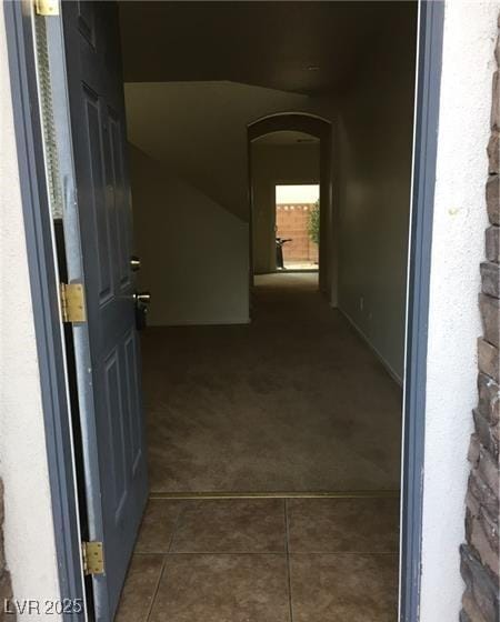 hallway with dark tile patterned floors, arched walkways, and dark colored carpet