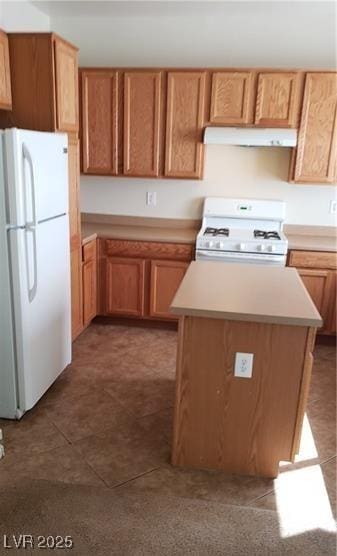 kitchen featuring dark tile patterned flooring, white appliances, light countertops, and under cabinet range hood