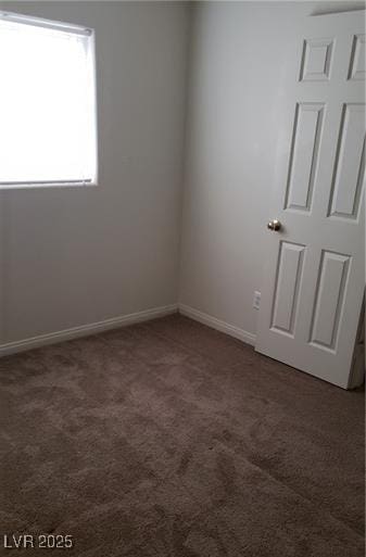 unfurnished room with dark carpet and baseboards