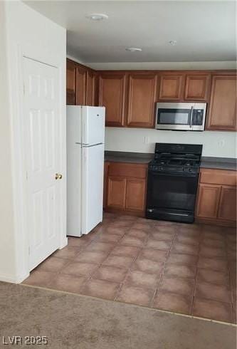 kitchen with dark countertops, stainless steel microwave, black gas range oven, brown cabinetry, and freestanding refrigerator