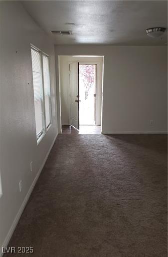 spare room featuring dark colored carpet, visible vents, and baseboards