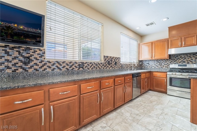 kitchen featuring decorative backsplash, appliances with stainless steel finishes, brown cabinetry, a sink, and under cabinet range hood