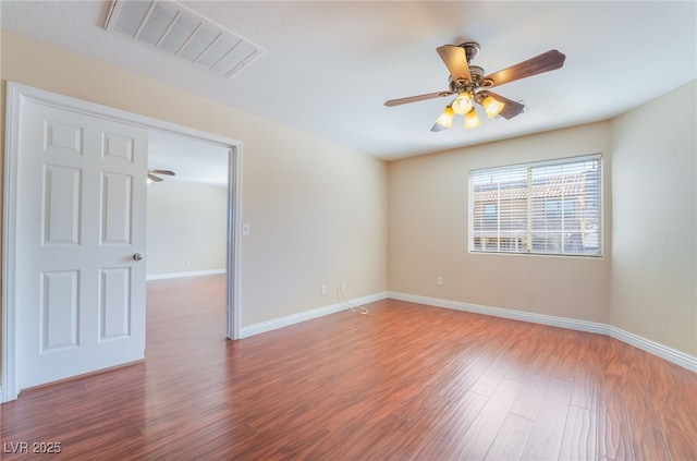 unfurnished room with ceiling fan, wood finished floors, visible vents, and baseboards