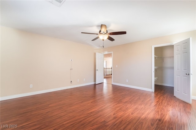 unfurnished bedroom featuring ceiling fan, wood finished floors, visible vents, baseboards, and a spacious closet