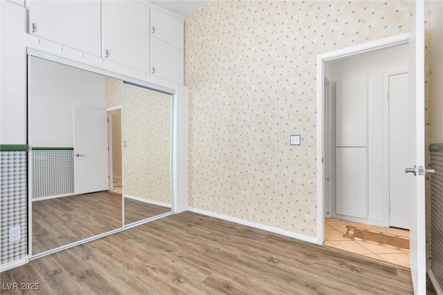 interior space featuring baseboards, light wood finished floors, a closet, and wallpapered walls