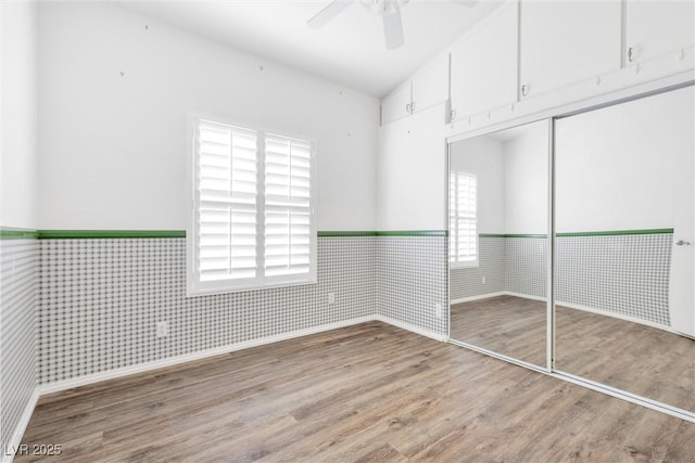 unfurnished bedroom with lofted ceiling, a wainscoted wall, wood finished floors, a ceiling fan, and a closet