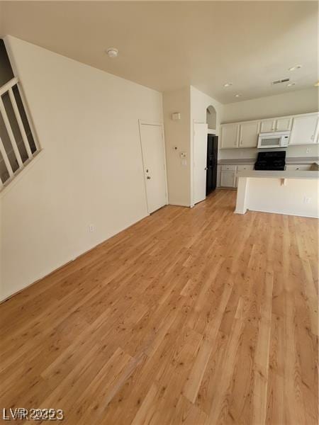 kitchen featuring white microwave, light wood-style floors, white cabinets, light countertops, and freestanding refrigerator