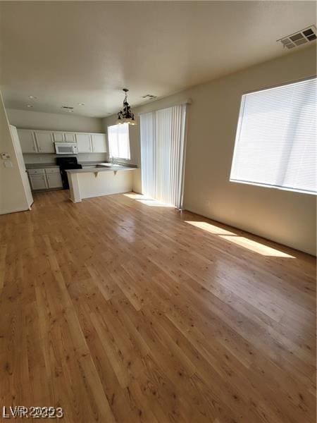 unfurnished living room with light wood-style floors, visible vents, and a notable chandelier