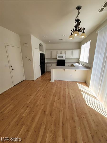 kitchen featuring decorative light fixtures, light wood finished floors, white microwave, white cabinetry, and a peninsula