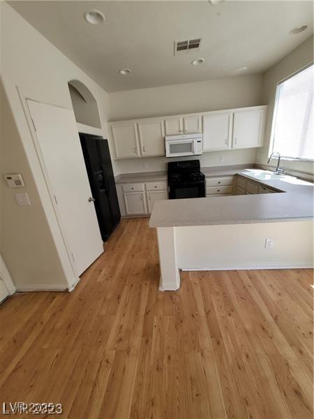 kitchen featuring visible vents, white cabinets, a peninsula, black appliances, and a sink