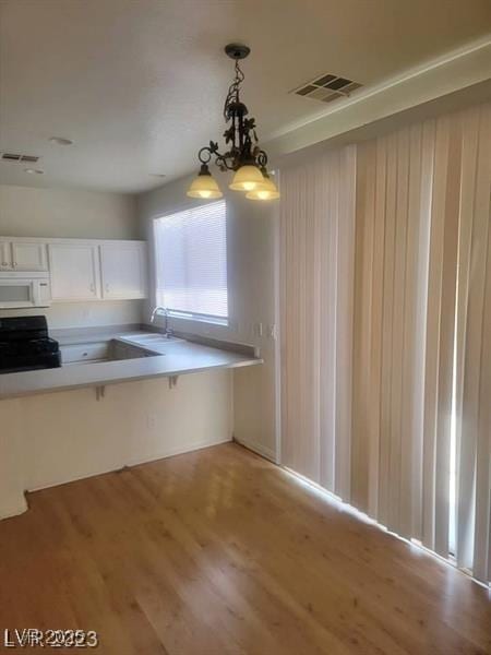 kitchen with white microwave, a sink, visible vents, hanging light fixtures, and range