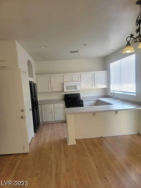 kitchen featuring light wood-style flooring, a peninsula, black appliances, white cabinetry, and a sink