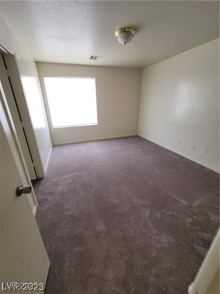 carpeted empty room featuring a textured ceiling, visible vents, and baseboards