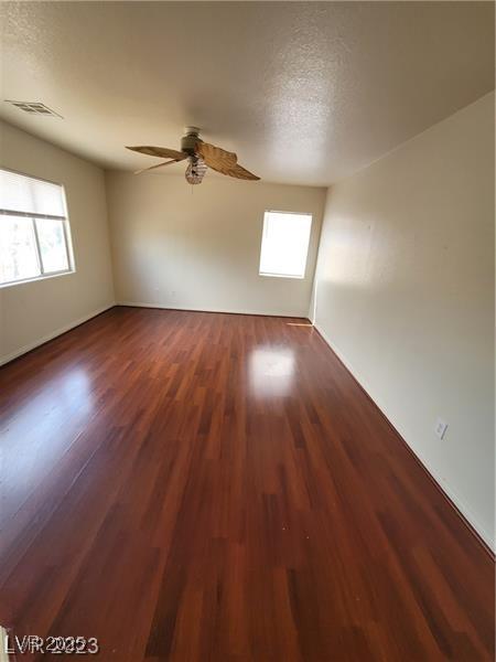 unfurnished room with a ceiling fan, wood finished floors, visible vents, and a healthy amount of sunlight