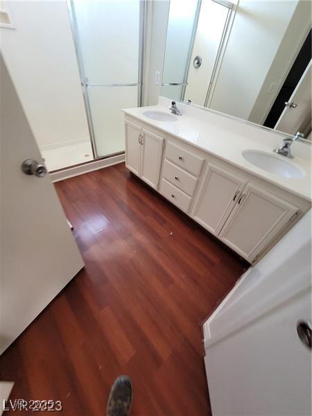 bathroom featuring double vanity, wood finished floors, a sink, and a shower with door