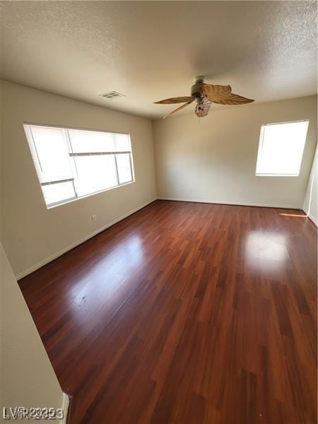 spare room with dark wood-style flooring, visible vents, ceiling fan, a textured ceiling, and baseboards