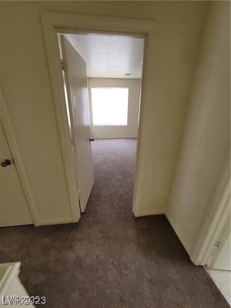 hall featuring dark carpet and a textured ceiling