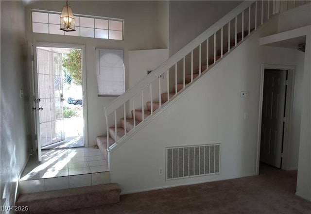 foyer entrance featuring carpet, visible vents, stairway, and a towering ceiling