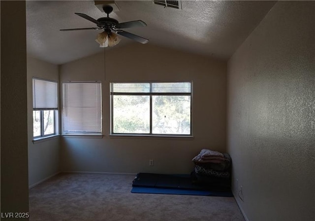 carpeted empty room featuring a ceiling fan, visible vents, vaulted ceiling, and a textured ceiling