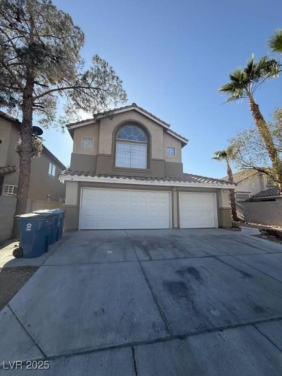 traditional home featuring a tile roof, driveway, an attached garage, and stucco siding