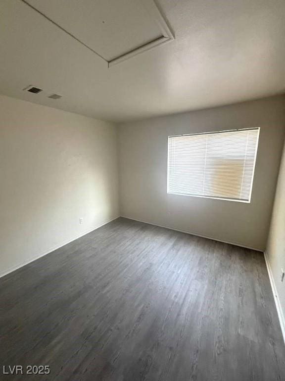 spare room featuring dark wood-type flooring, visible vents, and attic access