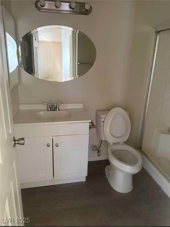 bathroom with toilet, wood finished floors, vanity, baseboards, and a shower stall