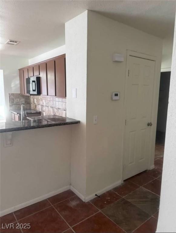 kitchen with dark tile patterned flooring, visible vents, backsplash, stainless steel microwave, and dark countertops