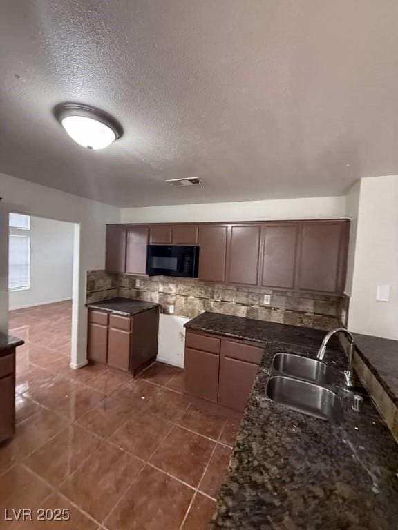 kitchen with tasteful backsplash, dark countertops, a textured ceiling, black microwave, and a sink