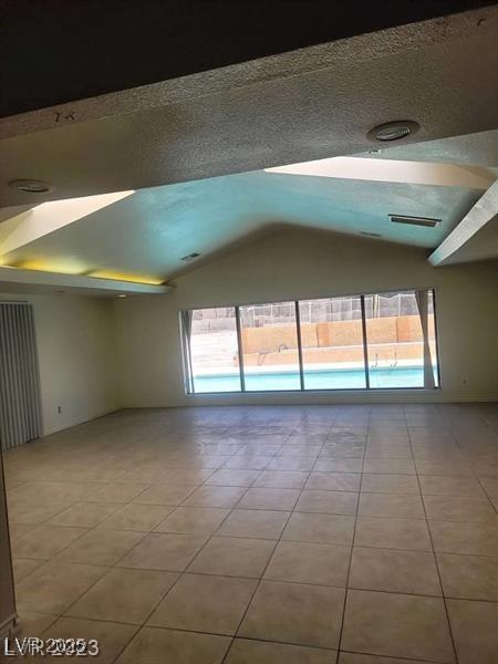 tiled empty room featuring lofted ceiling, plenty of natural light, visible vents, and a textured ceiling