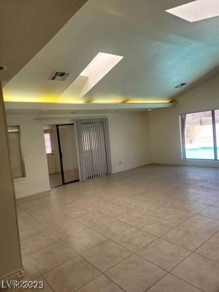 spare room featuring lofted ceiling with skylight, light tile patterned floors, and visible vents