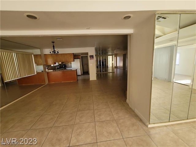 interior space with brown cabinets, light tile patterned floors, visible vents, freestanding refrigerator, and a chandelier