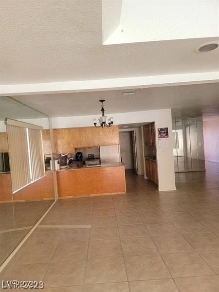 kitchen with a textured ceiling, a peninsula, light tile patterned flooring, and a notable chandelier