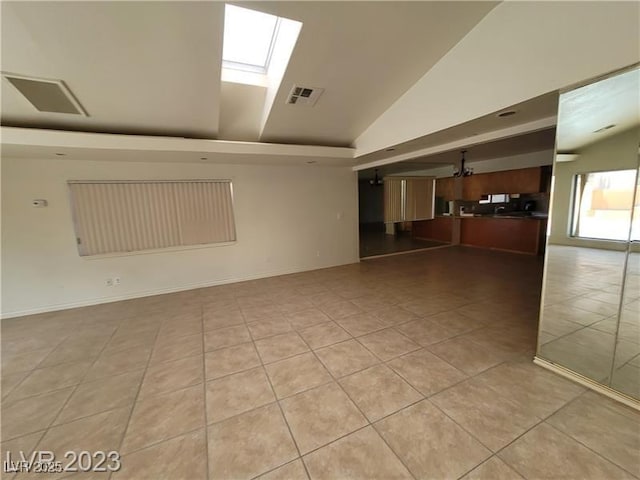 spare room with vaulted ceiling with skylight, light tile patterned flooring, visible vents, and baseboards