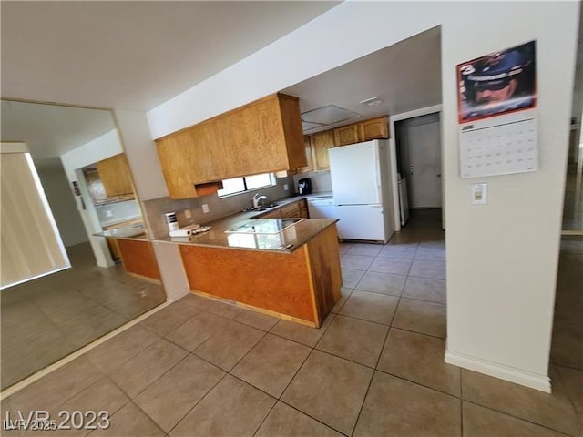 kitchen featuring light tile patterned floors, black electric stovetop, a peninsula, freestanding refrigerator, and brown cabinetry