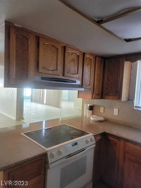 kitchen with under cabinet range hood, brown cabinetry, white range with electric cooktop, and light countertops